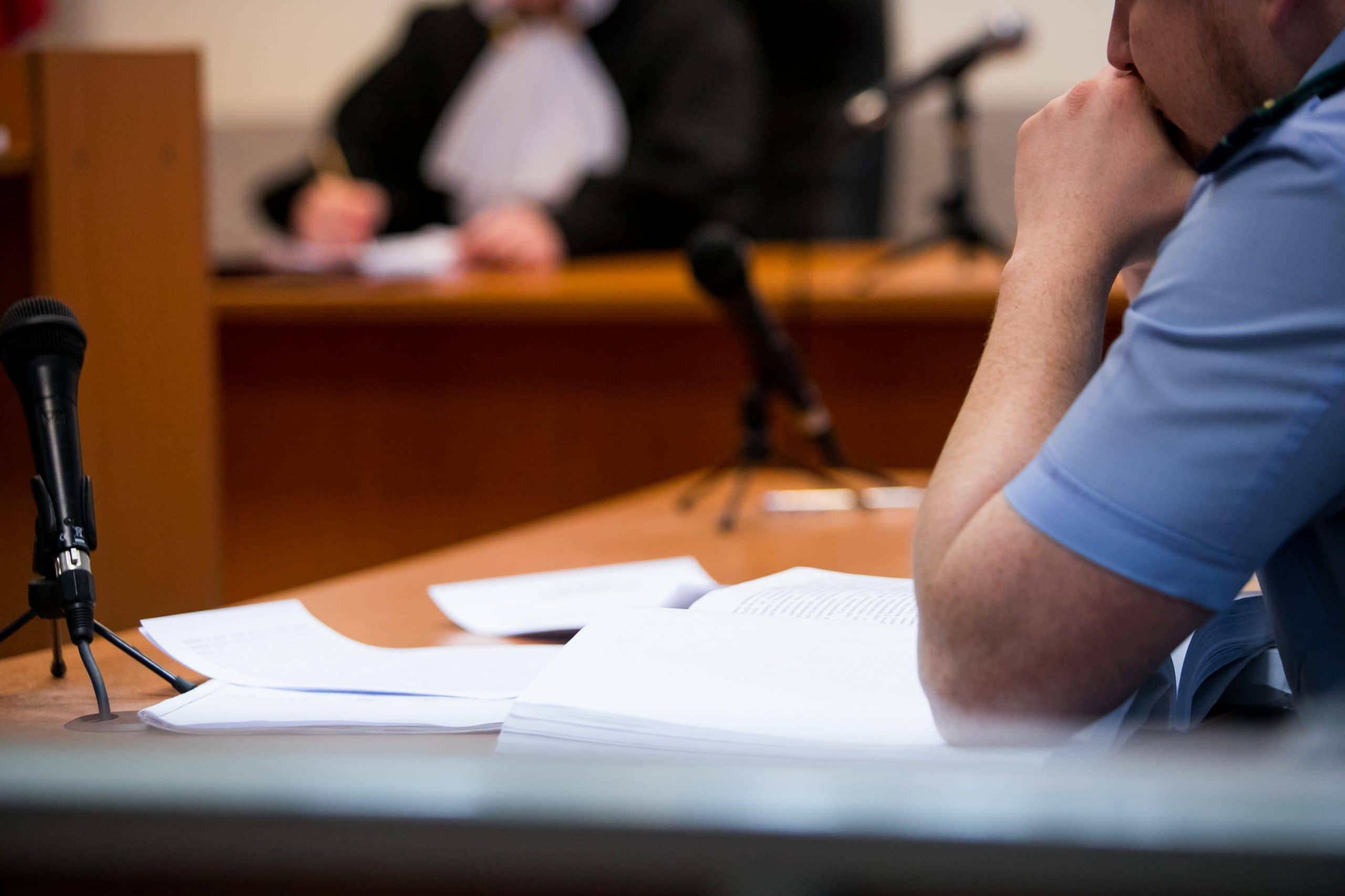 Courtroom setting during an ALR hearing after DWI, featuring a microphone, legal documents on the table, and a person in a blue shirt with a contemplative posture.